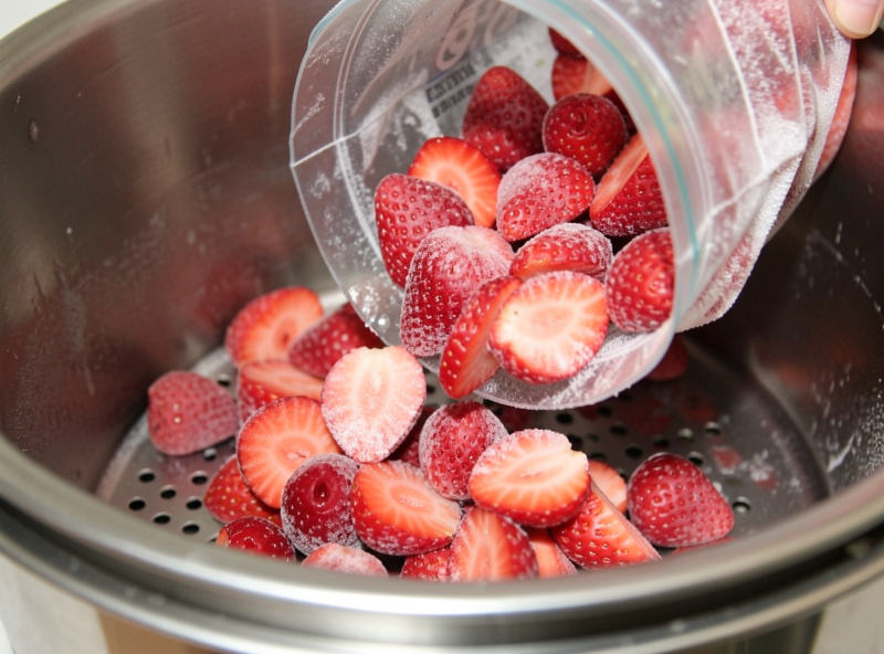 A bag of frozen sliced strawberries being poured into a freeze dryer tray for a first batch