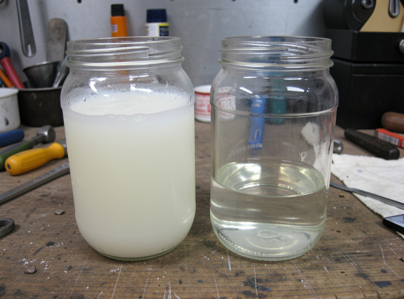 Cloudy milky used vacuum pump oil compared with clear fresh oil in two jars