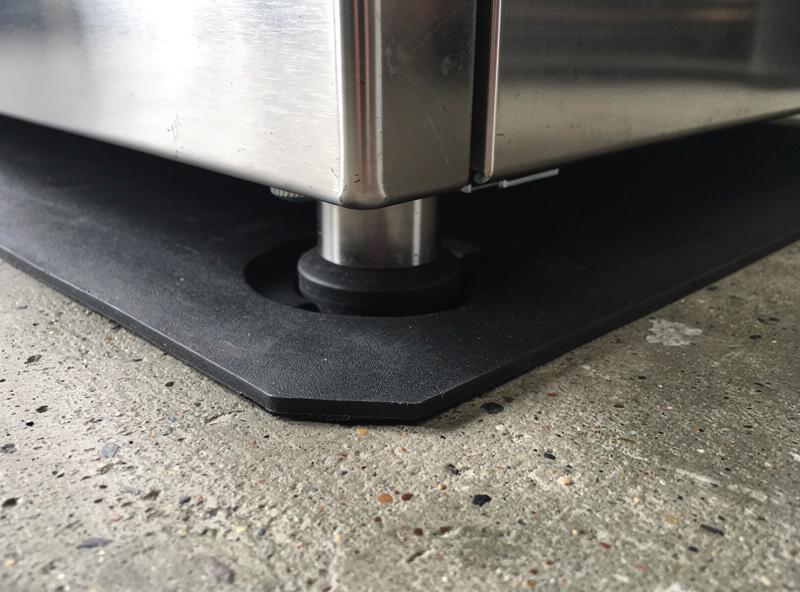 An anti-vibration mat under the foot of a heavy appliance on a concrete floor
