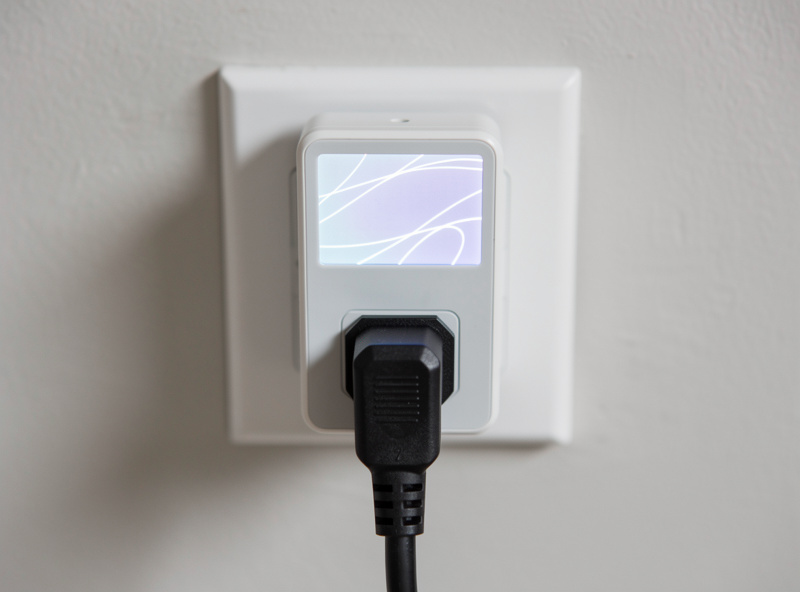 A plug-in kilowatt-hour energy monitor between a wall socket and an appliance plug
