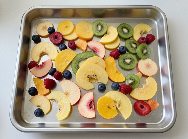 Sliced fruit spread flat on a stainless sheet pan ready to freeze loose before freeze drying
